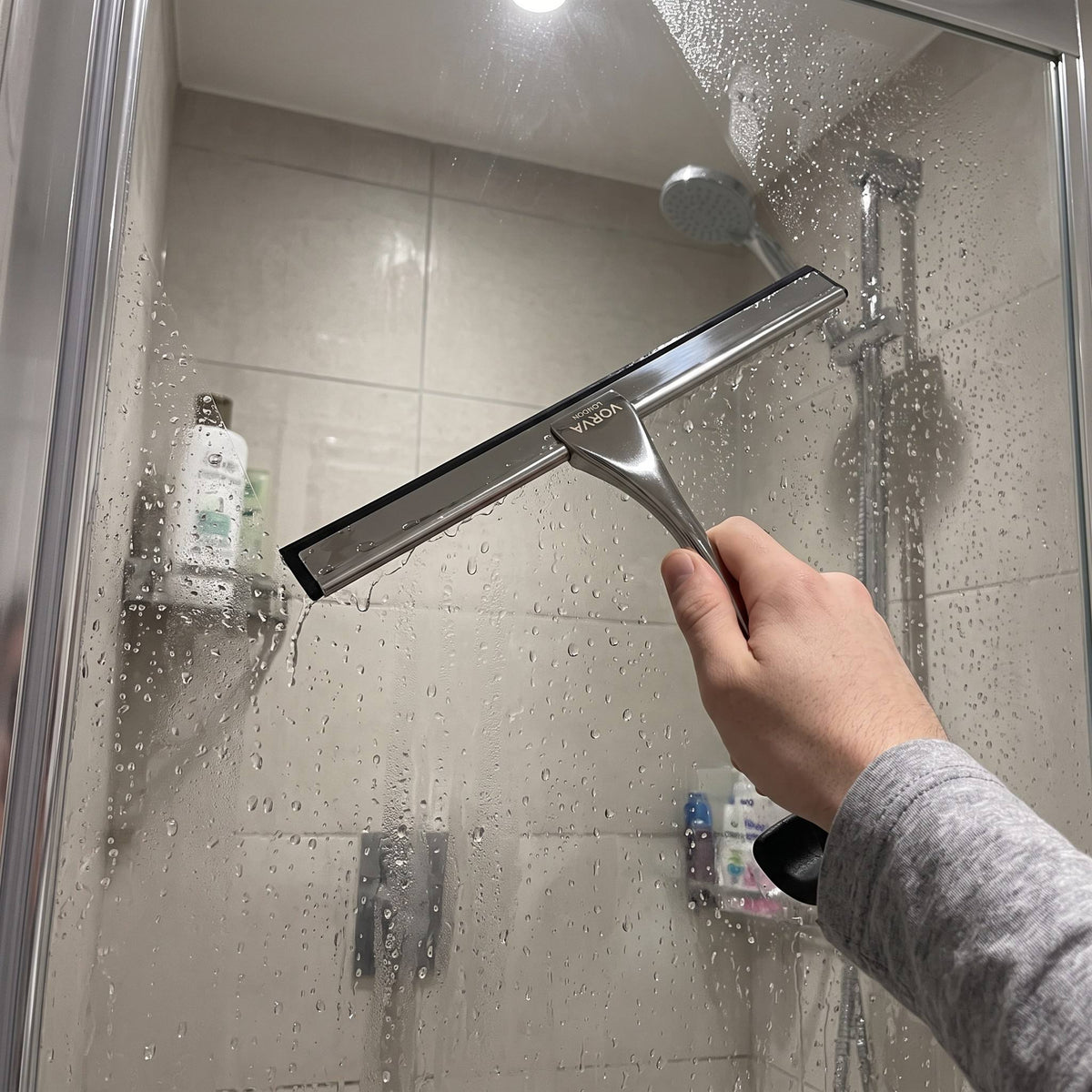 Hand using the VORVA LONDON squeegee to clean a wet glass shower door